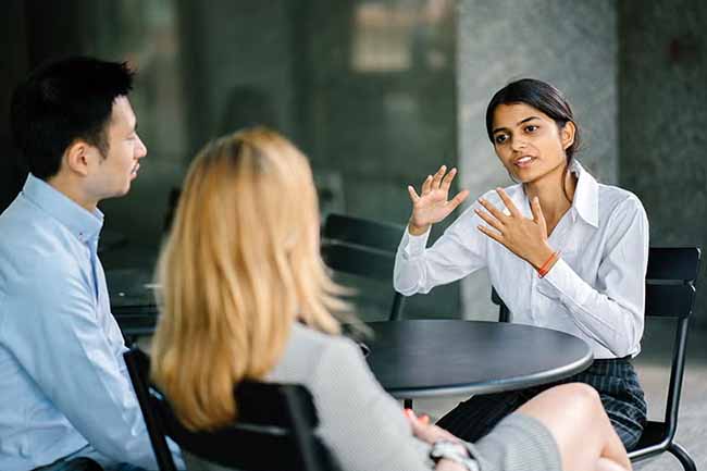 Three professionals discussing documents in a modern office lounge area.