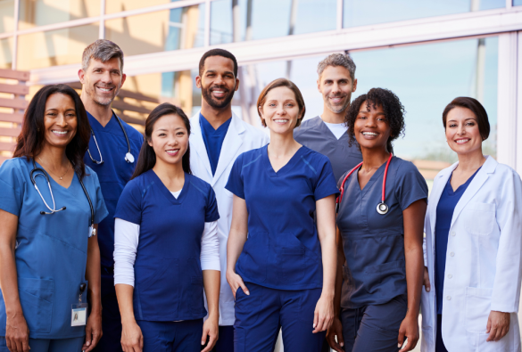 A diverse group of medical professionals smile at the camera while standing outside a building.