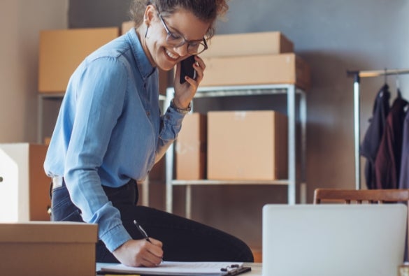 A VU Online MBA student smiles and talks on the phone at their desk.