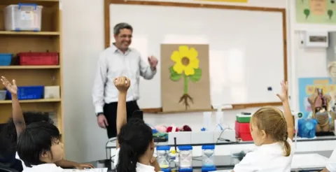 Dedicated primary school teacher assisting young students with interactive learning activities in a classroom.