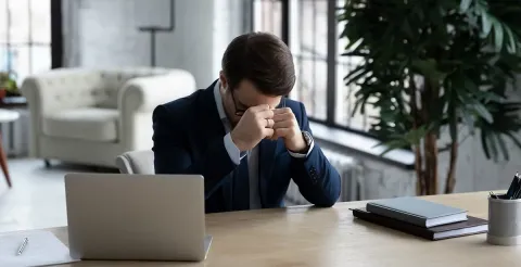 A professional looking discouraged while viewing a screen displaying rescinded job offer notifications.