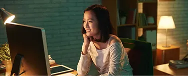 1. A woman seated at a desk, focused on her computer screen, with a notepad and pen beside her.
