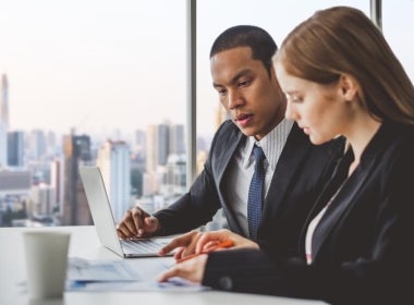 Two financial planners sit at a desk and discuss their work.