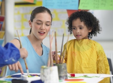 A primary school teacher teaching a student to paint.