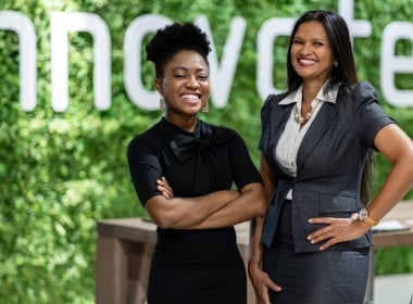 Two business leaders stand in front of a sign that says ‘innovation.’