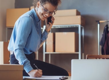A VU Online MBA student smiles and talks on the phone at their desk.