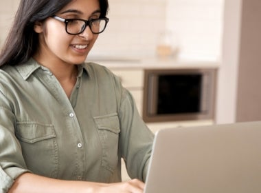 A VU Online Master of Public Health student is sitting at a table, working on her laptop and smiling.