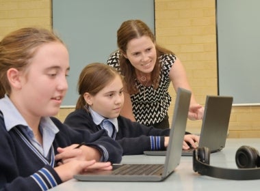 A primary school teacher with a student, pointing at something on their laptop.