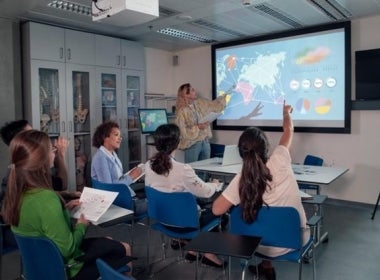 A public health educator gives a presentation on international healthcare using a world map.