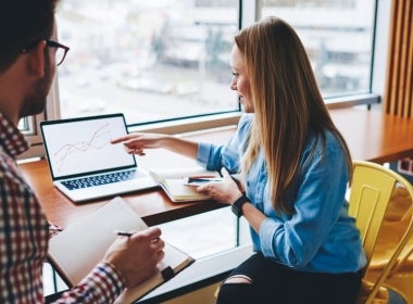 A digital marketing manager and MBA graduate presenting a power point to a colleague in a cafe.
